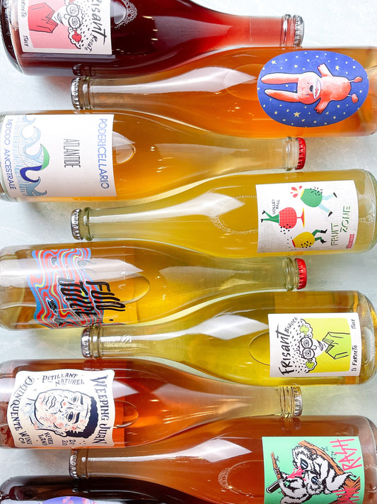 A colorful array of natural wine bottles with fanciful label designs, laid all in a row.